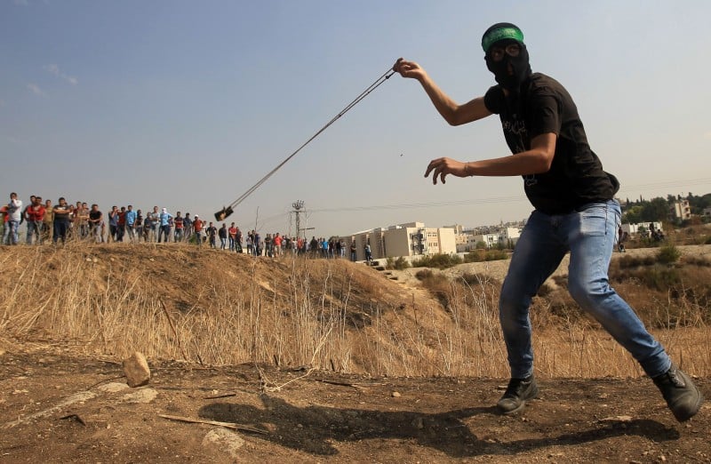 Palestinos utilizam estilingues para arremessar pedras contra as forças militares israelenses