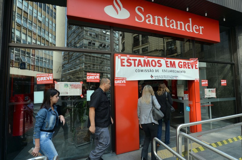  PEOPLE ENTER TO USE ATMS AT A CLOSED BANK BRANCH WITH POSTERS READING "WE ARE ON STRIKE" IN DOWNTOWN SAO PAULO, BRAZIL ON OCTOBER 6 2015. THE EMPLOYEES OF BRAZILIAN BANKS WENT ON INDEFINITE STRIKE IN DEMAND OF A WAGE INCREASE OF 16%. AFP PHOTO / NELSON ALMEIDA  