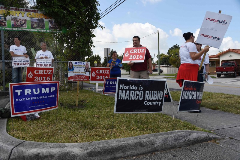  Supporters hold signs for Republican candidates in front of polling precinct for the Florida Primary on March 15, 2016 in Miami, Florida.   Voters began going to the polls Tuesday in five make-or-break presidential nominating contests, with Republican Donald Trump and Democrat Hillary Clinton seeking to tighten their grip as their party's front runners. / AFP PHOTO / RHONA WISE  