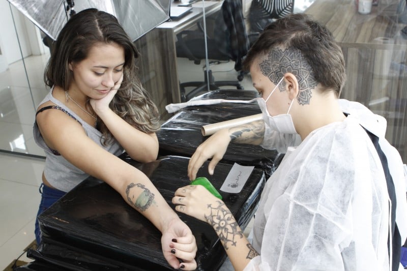 Lara Almeida (e) em atendimento com a tatuadora Brenda Sloczuk