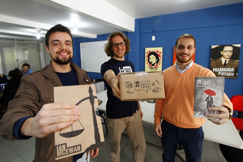 Os três sócio-fundadores da Tag Livros: Arthur Dambros (camisa Azul-escuro), Gustavo Lembert da Cunha (blusão laranja) e Tomás Susin dos Santos com as caixinhas dos livros que eles comercializam