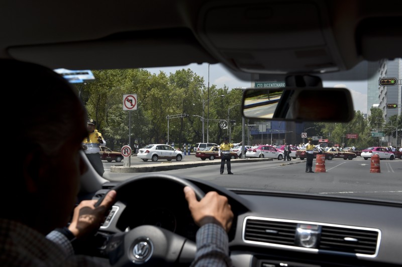  A DRIVER OF THE PRIVATE TAXI COMPANY UBER IS DIVERTED BY TRAFFIC POLICE FROM INSURGENTES AVENUE AS TAXI DRIVERS CROSS THE AVENUE DURING A PROTEST AGAINST THE COMPANY FOR ALLEGED UNFAIR COMPETITION, IN MEXICO CITY ON MAY 25, 2015. THOUSANDS OF TAXI DRIVERS PROTESTED ACROSS THE MEXICAN CAPITAL TO DEMAND THE GOVERNMENT TO TAKE ACTION AGAINST UBER, WHILE THE COMPANY RETALIATES BY OFFERING FREE TRANSPORT IN THE CITY.   AFP PHOTO / YURI CORTEZ  