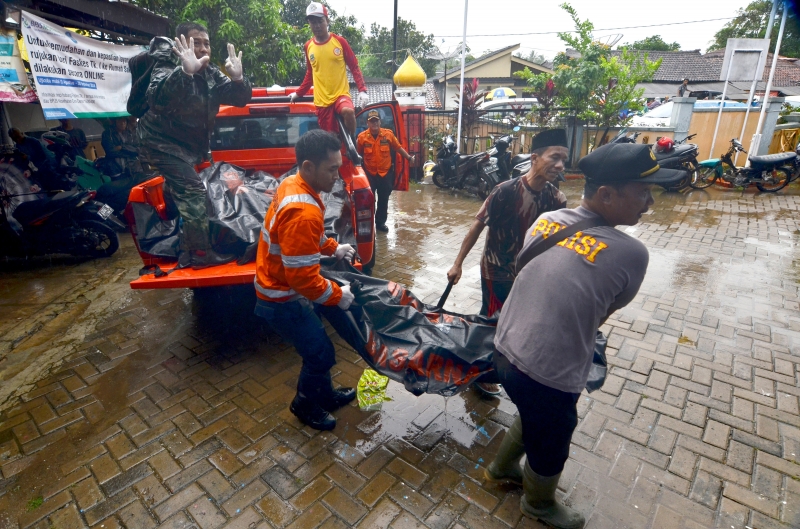 Rescuers carry body bags of victims to a makeshift mortuary in Carita on December 23, 2018, after the area was hit by a tsunami on December 22 following an eruption of the Anak Krakatoa volcano. - A tsunami following a volcanic eruption killed 62 people and injured hundreds more as it slammed without warning into tourist beaches and coastal areas around Indonesia's Sunda Strait on the night of December 22, sending panicked holidaymakers and residents fleeing. (Photo by Ronald / AFP)
      Caption