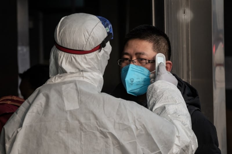 A security personnel wearing protective clothing to help stop the spread of a deadly virus which began in Wuhan, checks the temperature of a man at a subway station entrance in Beijing on January 27, 2020. - China on January 27 extended its biggest national holiday to buy time in the fight against a viral epidemic and neighbouring Mongolia closed its border, after the death toll spiked to 81 despite unprecedented quarantine measures. (Photo by NICOLAS ASFOURI / AFP)