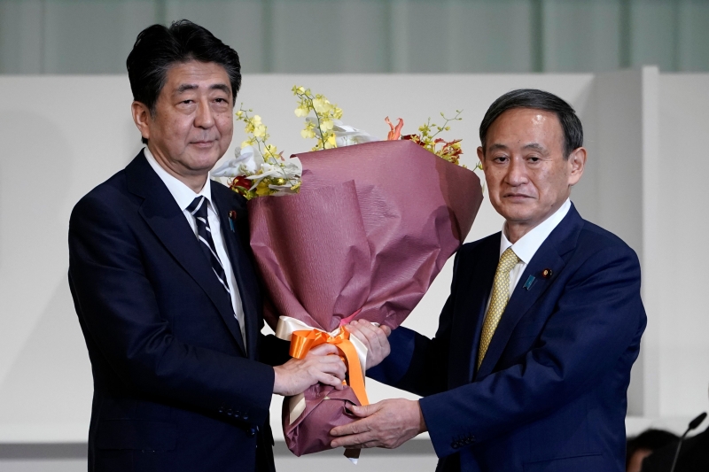 Yoshihide Suga (d) é assessor do primeiro-ministro Shinzo Abe (e)