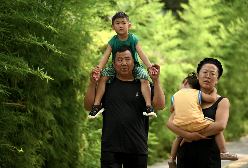  A man carries a child on his shoulders along a street in Beijing on August 2, 2022. - China's population will begin to shrink by 2025, officials said, as family sizes grow smaller and citizens age. (Photo by Noel Celis / AFP)