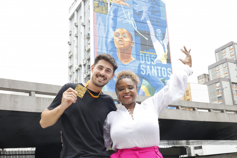 Daiane Dos Santos e Kelvin Koubik em frente ao mural que conta com 50 metros de altura
