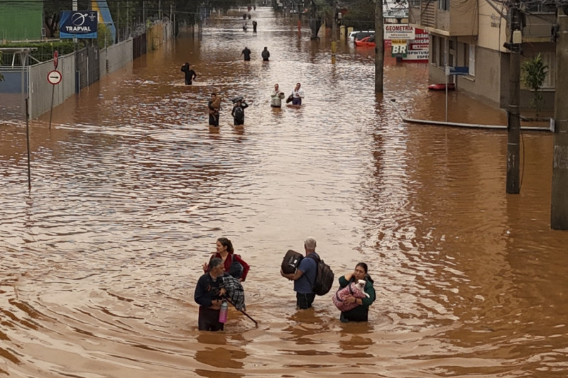  Aerial view of people walking through a flooded street at the Navegantes neighborhood in Porto Alegre, Rio da Grande do State, Brazil on May 4, 2024 - The floods caused by the intense rains that hit southern Brazil left at least 56 dead and 67 missing, according to a new report on Saturday from Civil Defense. (Photo by Carlos Fabal / AFP)
      Caption