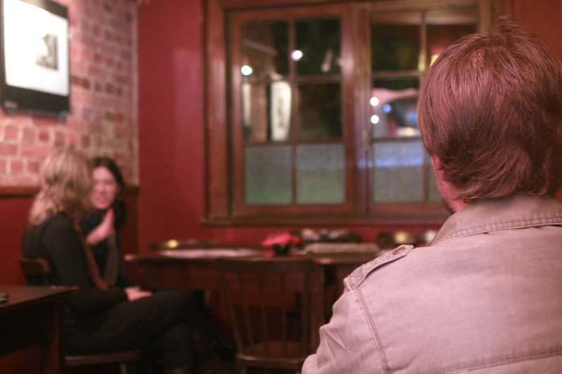 GRUPO DE MULHERES CONVERSANDO AO FUNDO E, NO PRIMEIRO PLANO DA IMAGEM, UM CARA SENTADO DE COSTAS PARA A FOTO E DE FRENTE PARA AS MO�AS SEM CORAGEM DE FALAR COM ELAS. HOMEM T�MIDO. TIMIDEZ EM BARES. FALTA DE CORAGEM EM INICIAR UM FLERTE. MODORRA. FLEUMA.